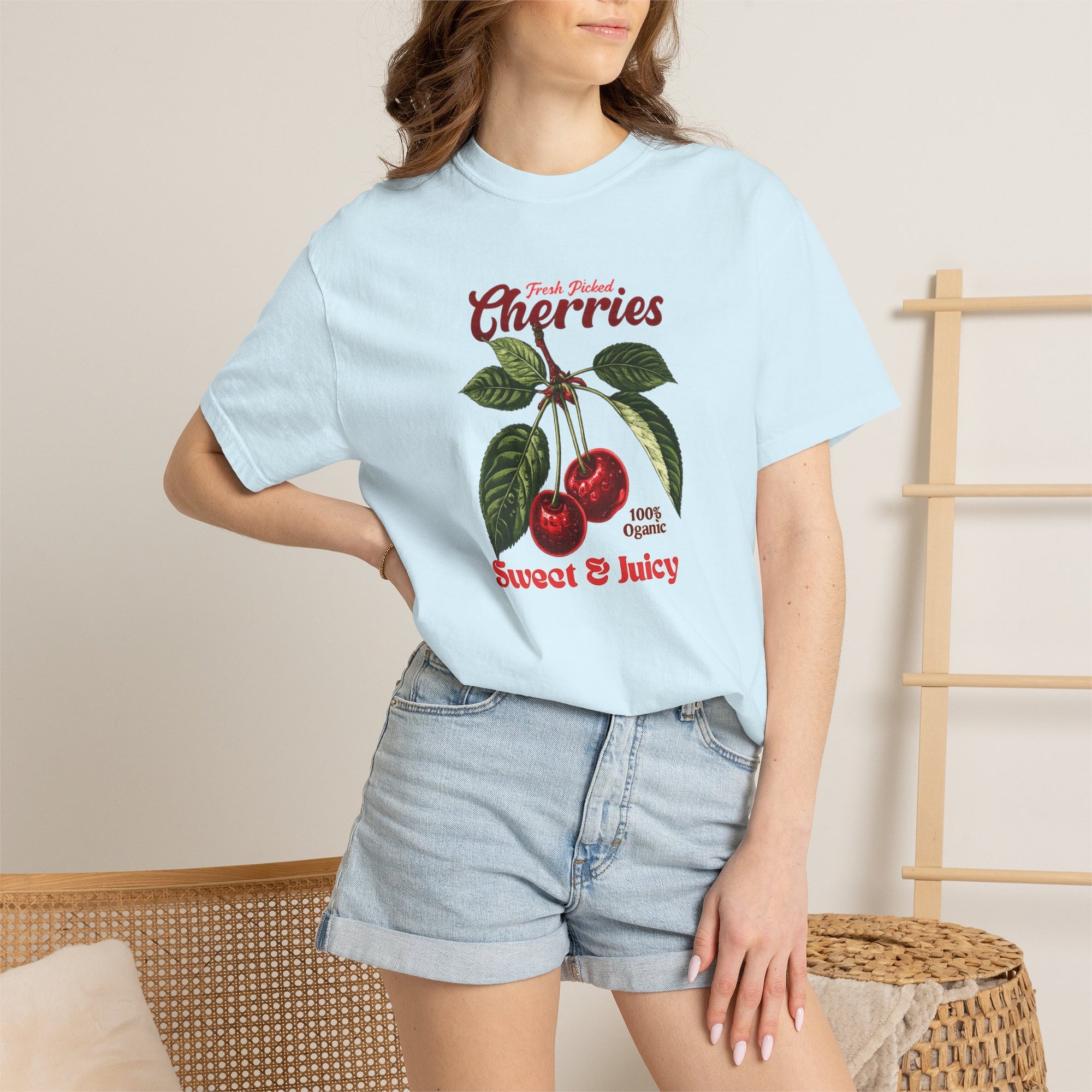 Heavyweight relaxed-fit T-shirt featuring a vintage-style botanical illustration of red cherries with green leaves and retro red script reading "Fresh Picked Cherries" and "Sweet & Juicy" on a plain background — Studio DeLuz graphic tee.