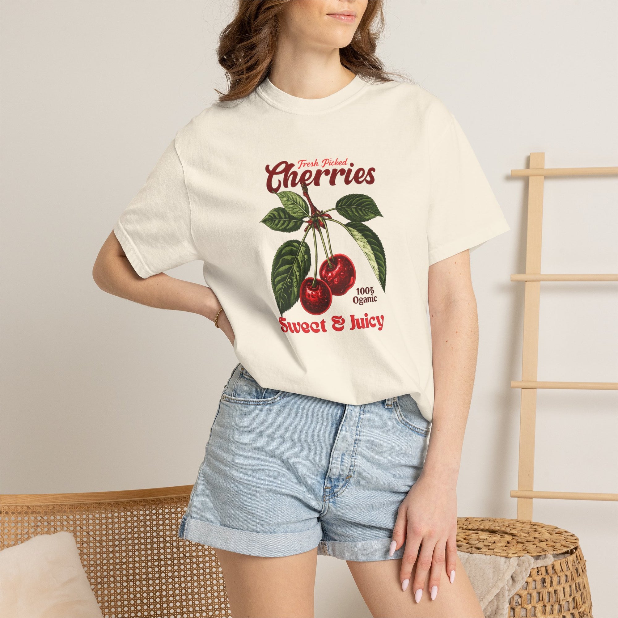 Heavyweight relaxed-fit T-shirt featuring a vintage-style botanical illustration of red cherries with green leaves and retro red script reading "Fresh Picked Cherries" and "Sweet & Juicy" on a plain background — Studio DeLuz graphic tee.