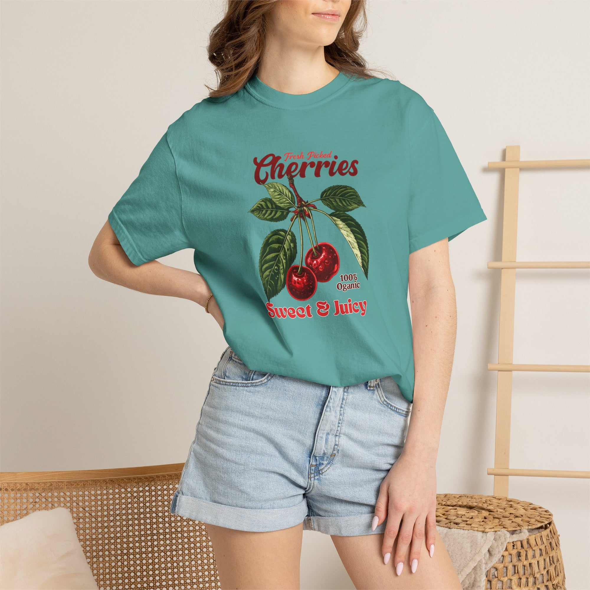 Heavyweight relaxed-fit T-shirt featuring a vintage-style botanical illustration of red cherries with green leaves and retro red script reading "Fresh Picked Cherries" and "Sweet & Juicy" on a plain background — Studio DeLuz graphic tee.