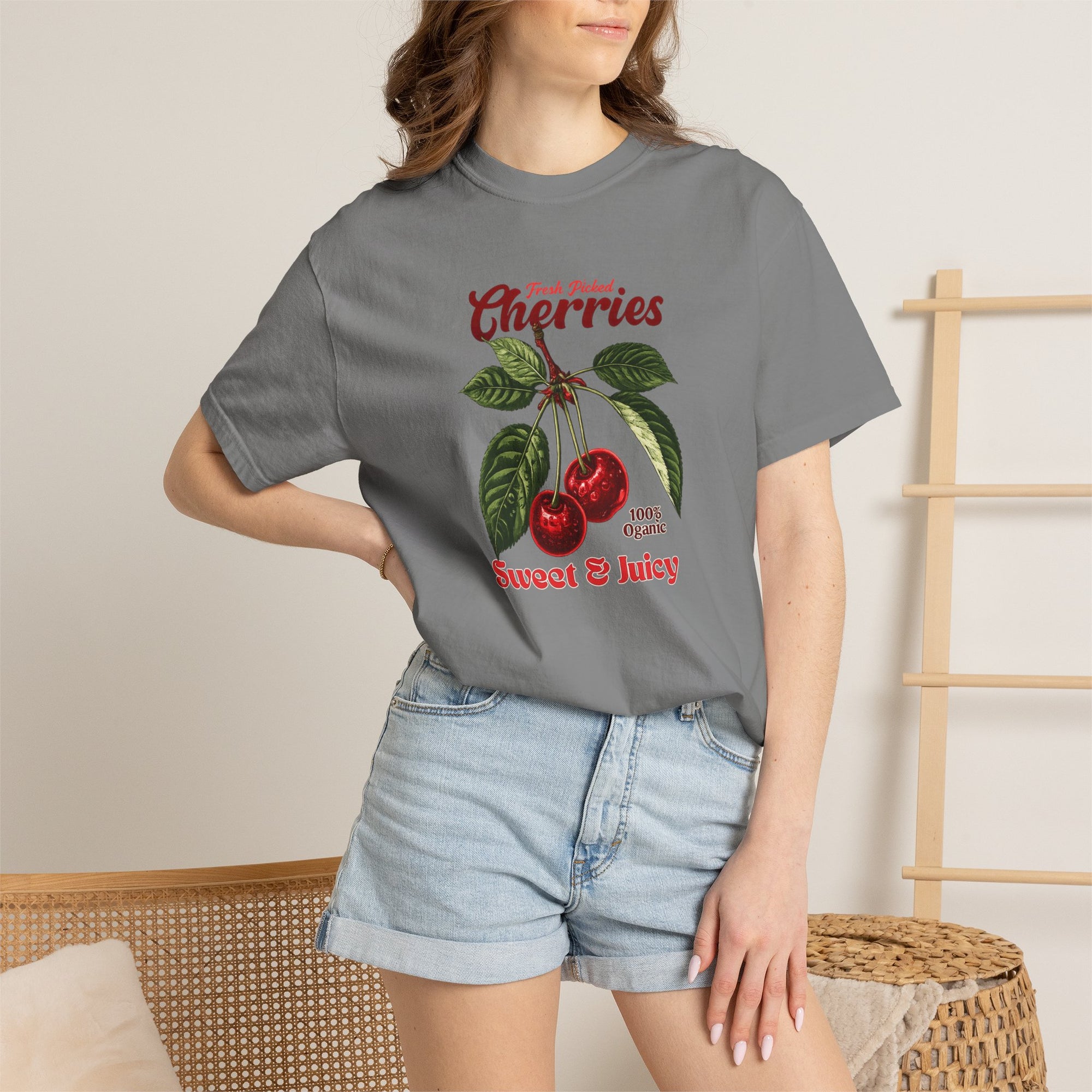 Heavyweight relaxed-fit T-shirt featuring a vintage-style botanical illustration of red cherries with green leaves and retro red script reading "Fresh Picked Cherries" and "Sweet & Juicy" on a plain background — Studio DeLuz graphic tee.